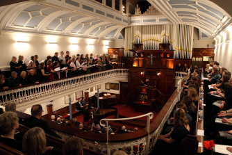 A view of a Welsh church from the gallery, with people sitting and watching a choir perform. A view of a Welsh church from the gallery, with people sitting and watching a choir perform.
