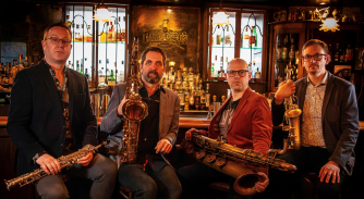 Four men holding saxophones look towards the camera. Four men holding saxophones look towards the camera.
