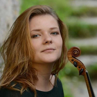 Maja Horvat looking into the camera holding a violin and wearing a black top.