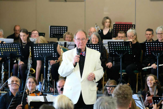 David Davies conductor, wearing a white jacket stands in front of members of Monmouth Concert Orchestra