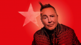 Nigel Kennedy in leather military jacket against a red background with a painted star