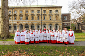 A choir standing in red cassocks and white surplices on grass
